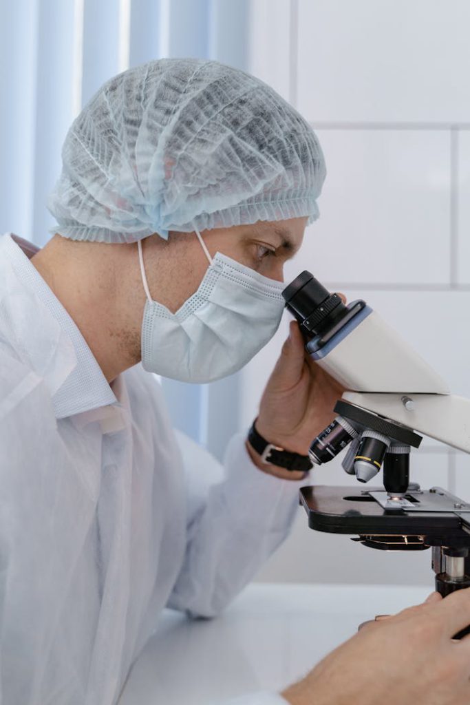 Scientist in laboratory gear examining a sample under a microscope indoors.